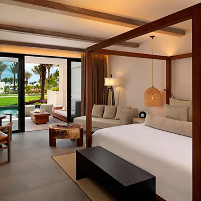 Luxury suite with garden and pool views, featuring a canopy bed, warm lighting, and terrace seating area.