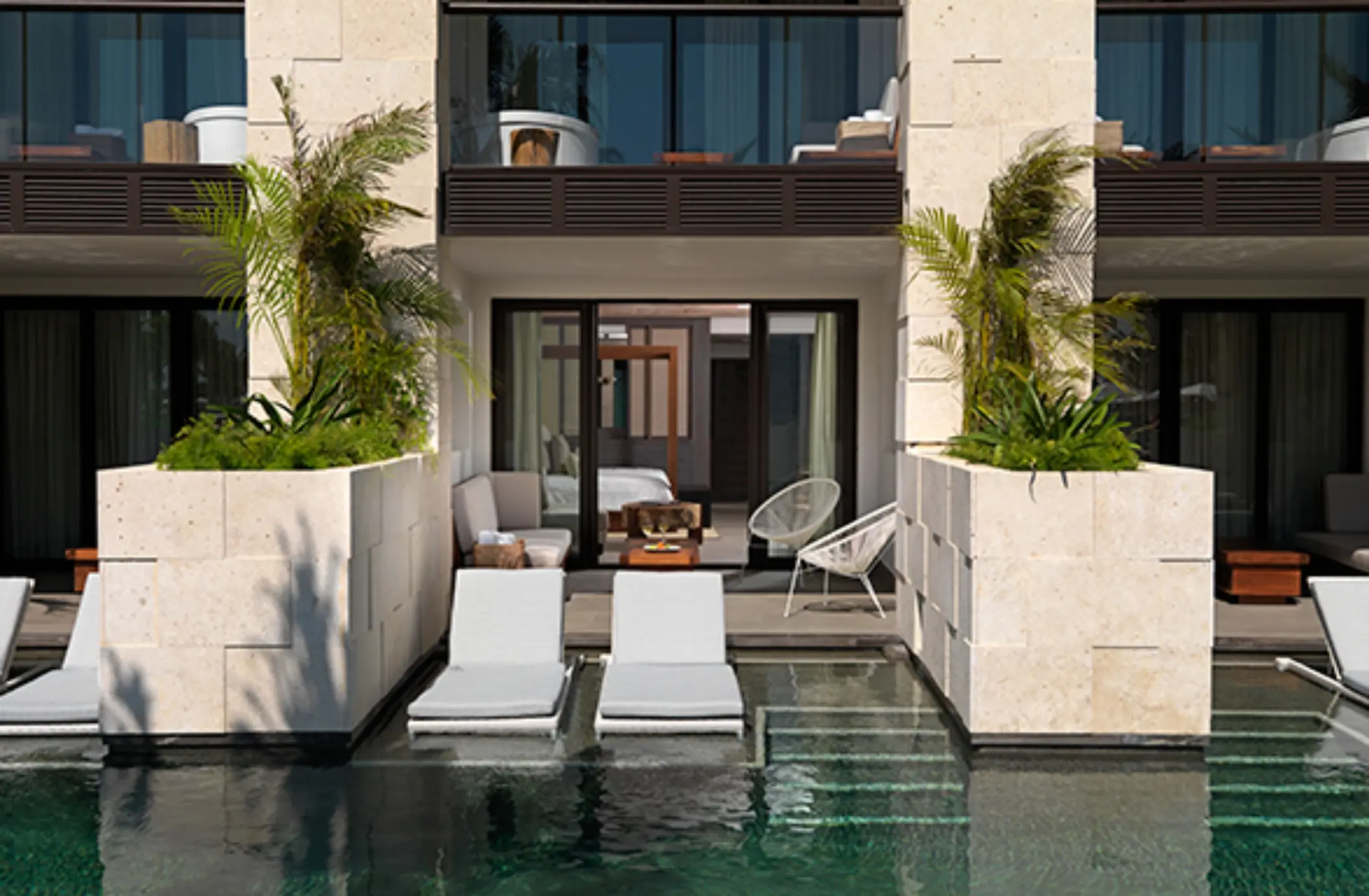 Swim-up suite terrace with lounge chairs in the pool, shaded patio seating, and sliding glass doors.
