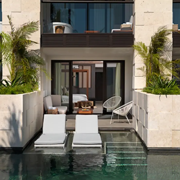 Swim-up suite terrace with lounge chairs in the pool, shaded patio seating, and sliding glass doors.