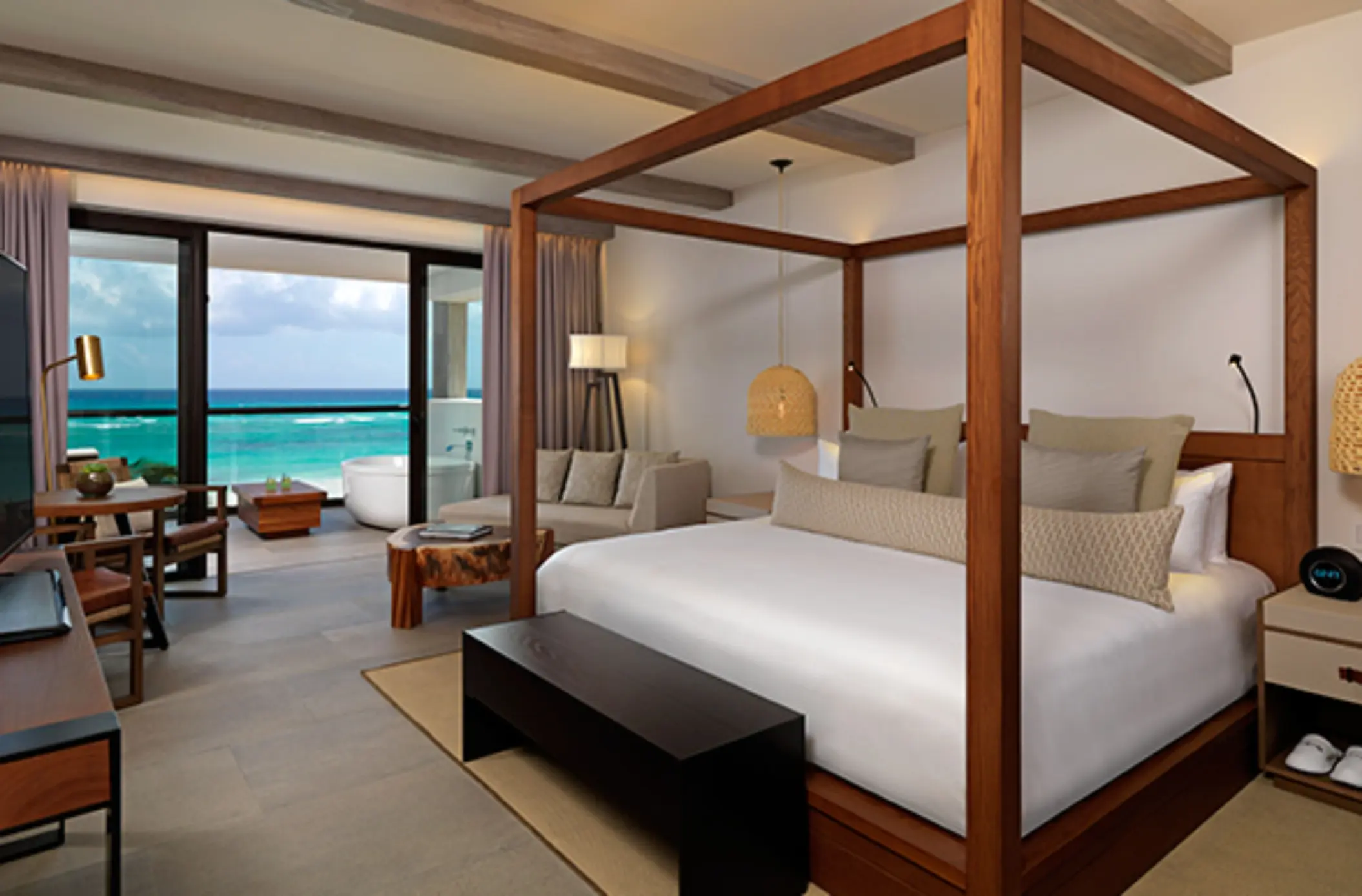 Spacious suite with canopy bed, seating area, and private balcony offering stunning views of the Caribbean Sea.