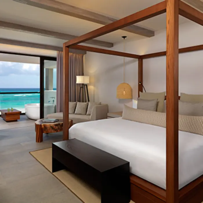 Spacious suite with canopy bed, seating area, and private balcony offering stunning views of the Caribbean Sea.