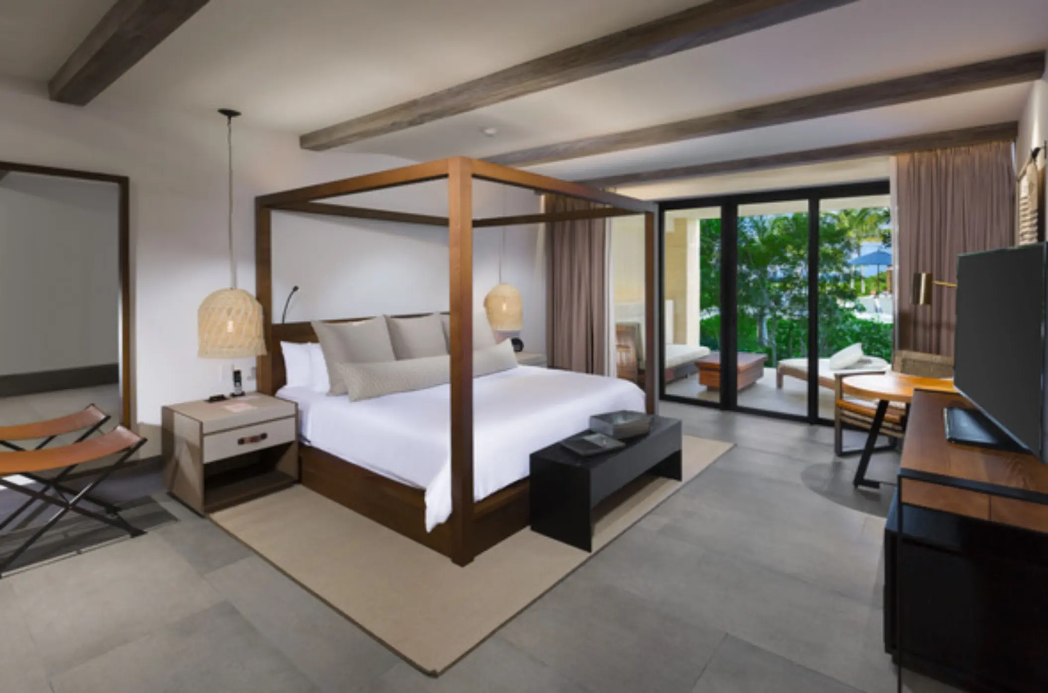Spacious suite with four-poster bed, private patio, and warm neutral tones blending indoor and outdoor comfort.