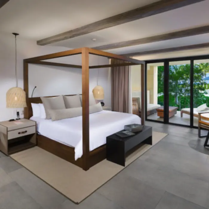 Spacious suite with four-poster bed, private patio, and warm neutral tones blending indoor and outdoor comfort.