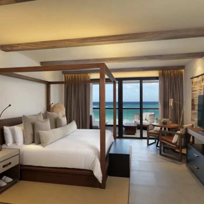 Oceanfront suite with king canopy bed, dining nook, and private balcony overlooking the Caribbean Sea.