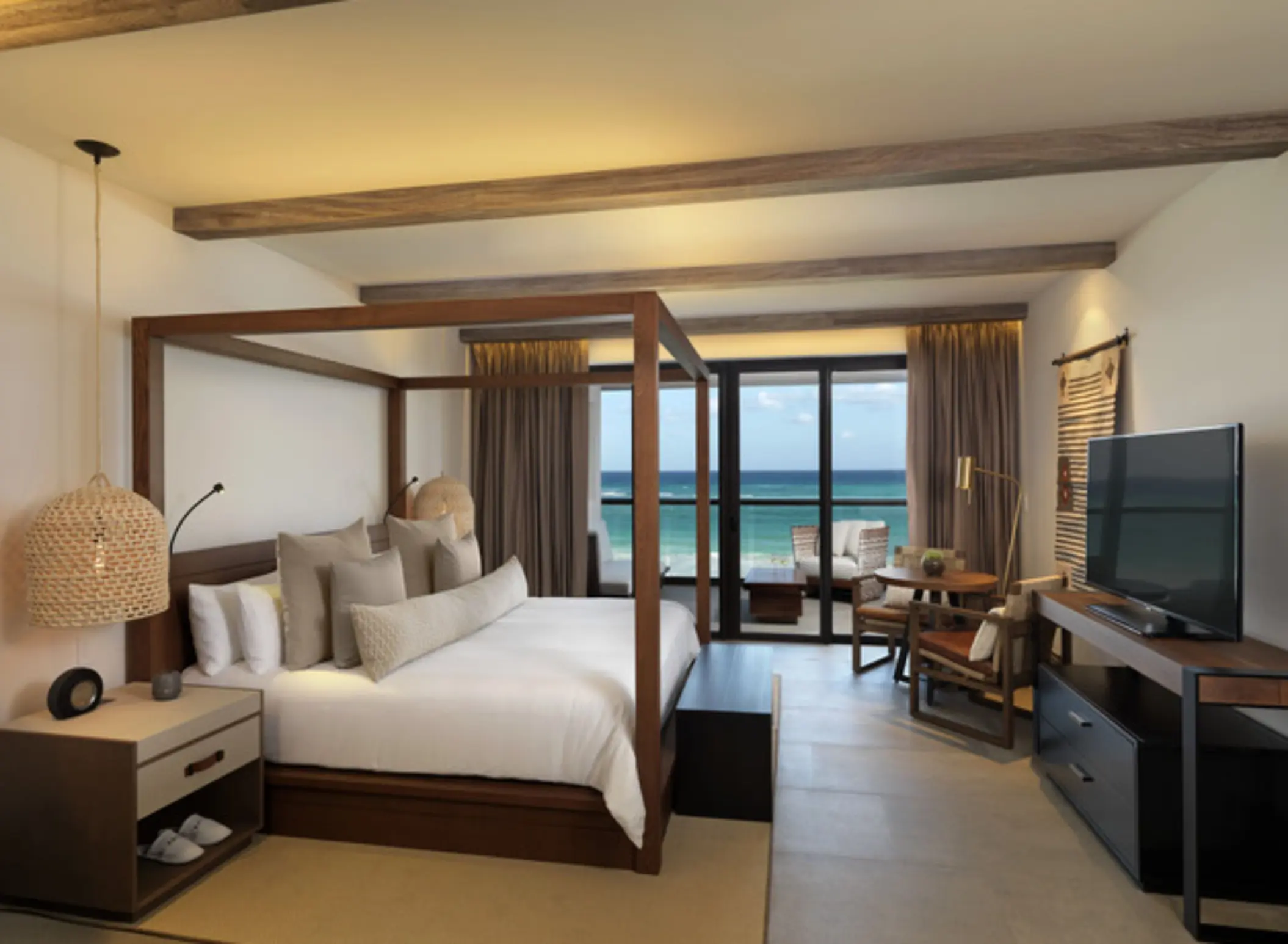 Oceanfront suite with king canopy bed, dining nook, and private balcony overlooking the Caribbean Sea.