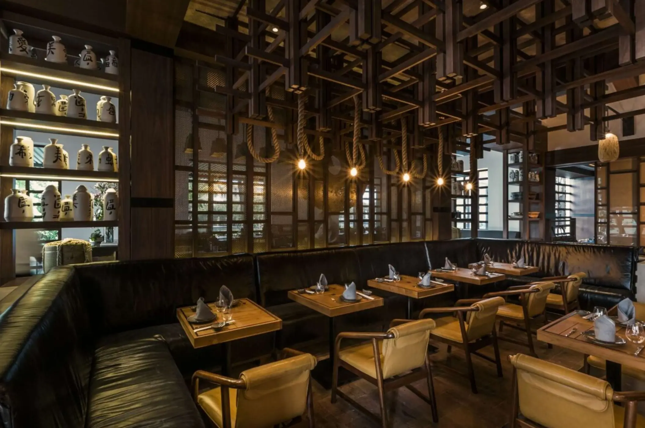 Dimly lit dining area with leather seating, wood grid ceiling, and small tables set for intimate meals.