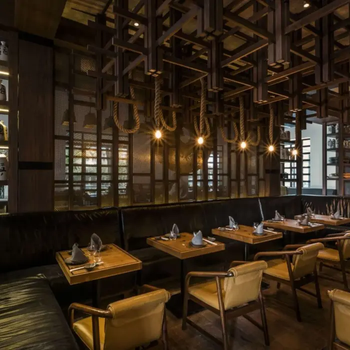 Dimly lit dining area with leather seating, wood grid ceiling, and small tables set for intimate meals.