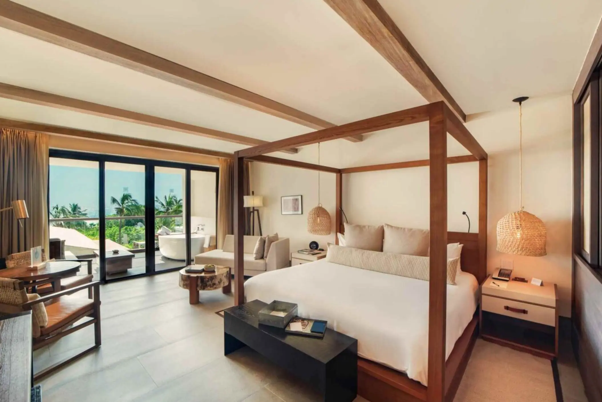 Bright and airy bedroom suite with canopy bed, seating area, and private balcony overlooking tropical greenery.