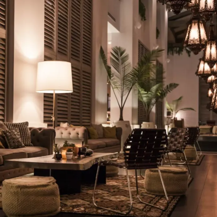 Chic hotel lounge at night with soft lighting, textured rugs, woven stools, and an inviting mix of seating.