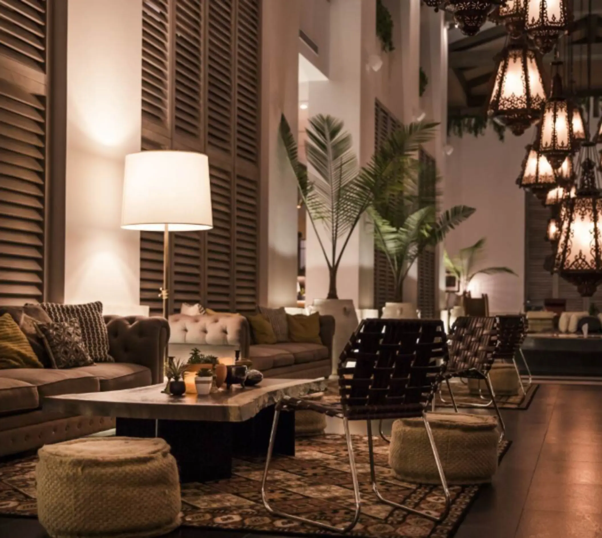 Chic hotel lounge at night with soft lighting, textured rugs, woven stools, and an inviting mix of seating.