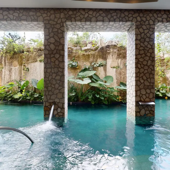 Stone-pillared hydrotherapy pool surrounded by lush vegetation and carved rock walls at Muluk Spa.