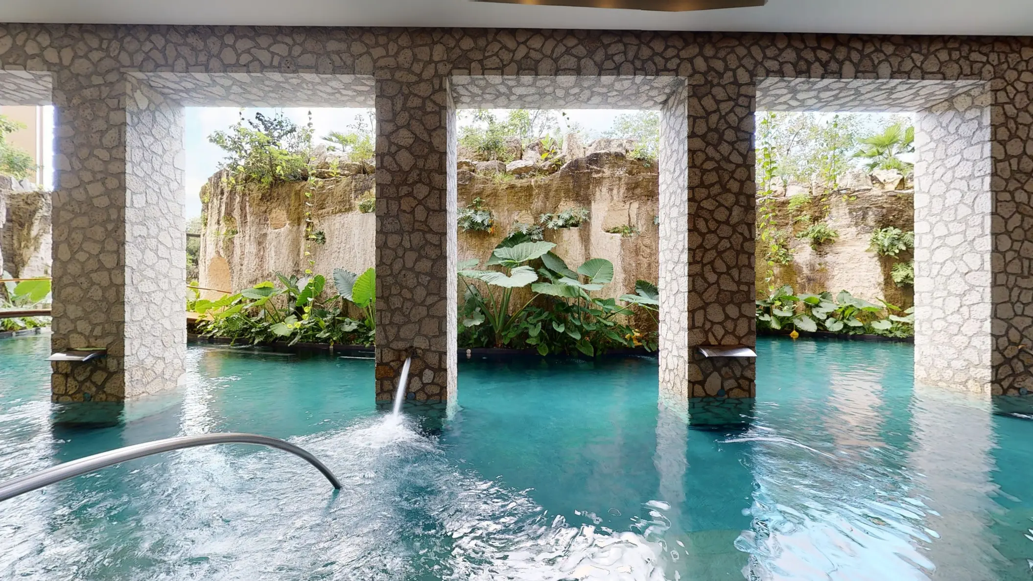 Stone-pillared hydrotherapy pool surrounded by lush vegetation and carved rock walls at Muluk Spa.