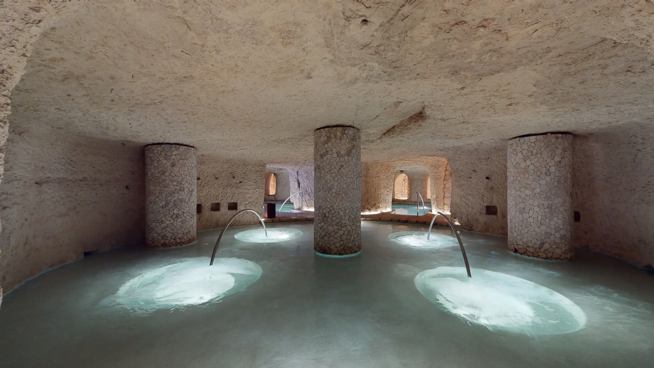 Underground circular hydrotherapy pool with stone columns and relaxing jets at Hotel Xcaret Arte.