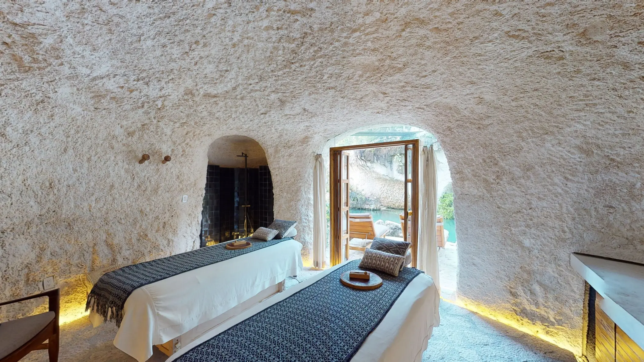 Spa cabin with massage beds inside a natural stone cave, opening to tranquil water views.
