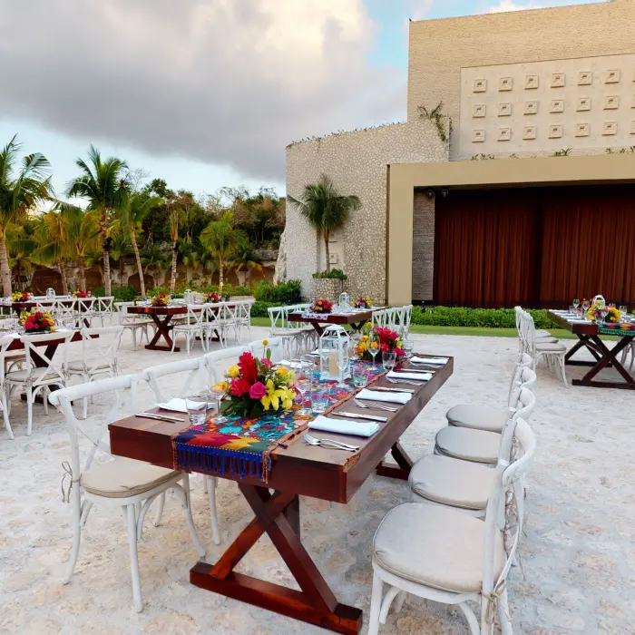 Outdoor wedding reception setup with long wooden tables, white chairs, and vibrant floral centerpieces.