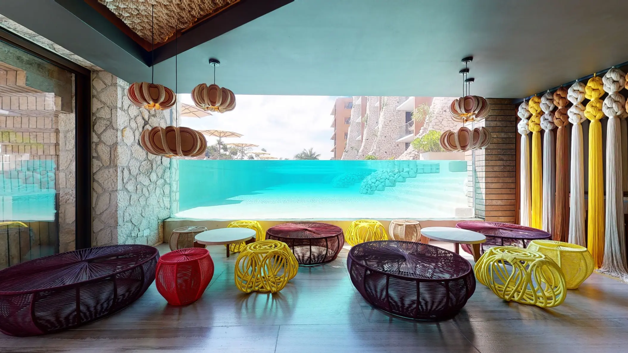 Colorful indoor lounge at Kibi-kibi with underwater pool view and woven furniture.