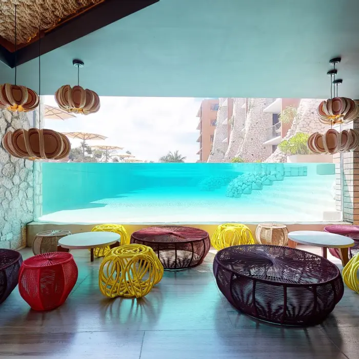 Colorful indoor lounge at Kibi-kibi with underwater pool view and woven furniture.