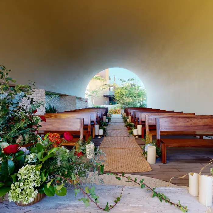 Indoor wedding chapel with arched ceiling, floral aisle décor, and wooden pews at Hotel Xcaret Arte.