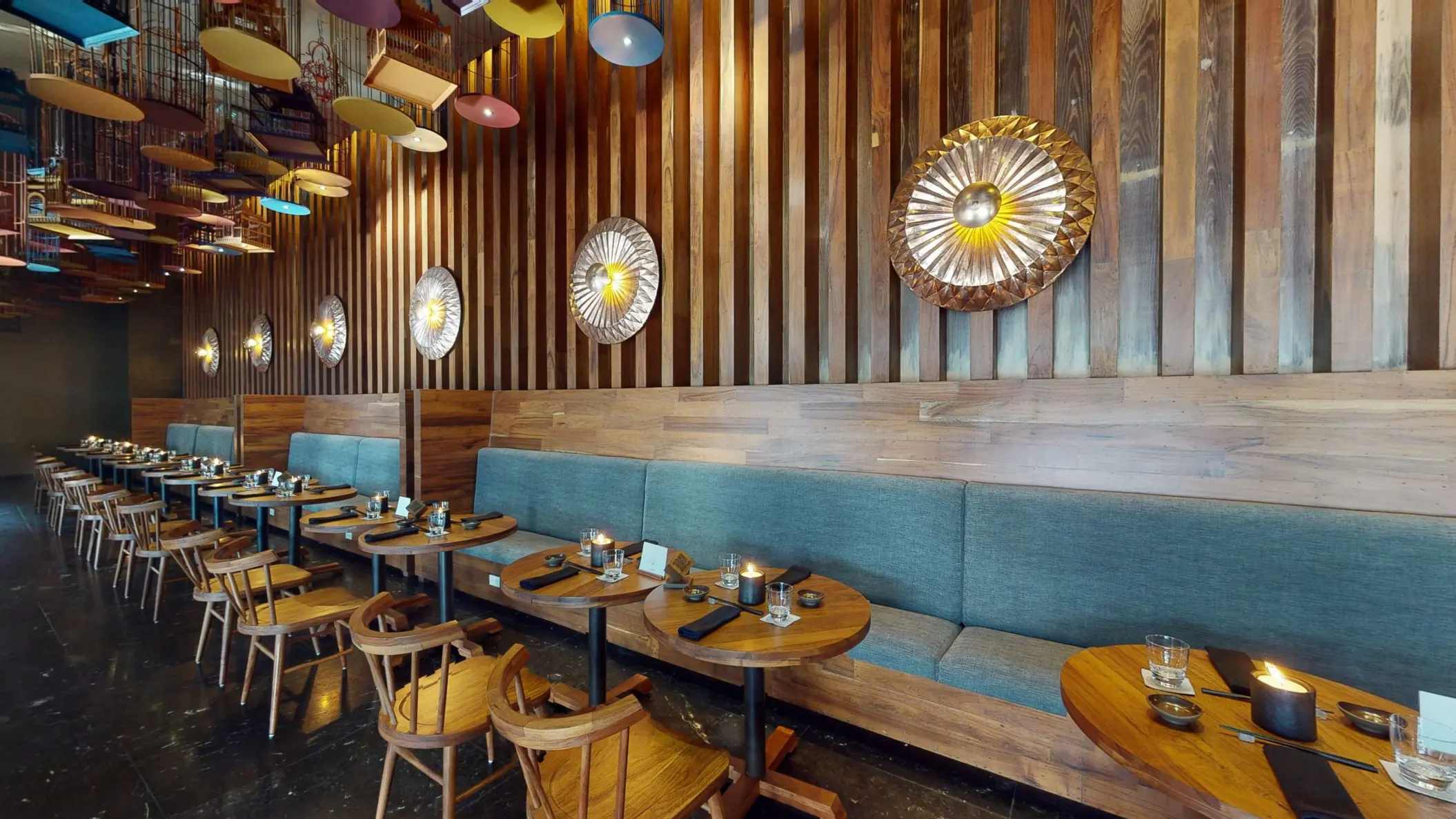Tah Xido restaurant seating with wood-paneled walls, teal booth seating, and round wooden tables.