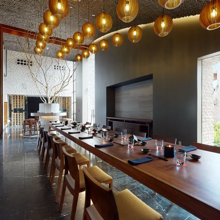 Elegant private dining room with a long wood table, pendant lights, and garden views through tall windows.