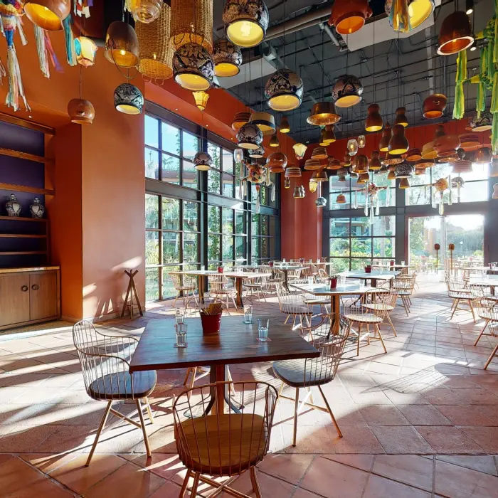 Bright, airy dining room with terracotta floors, floor-to-ceiling windows, and colorful hanging lights.