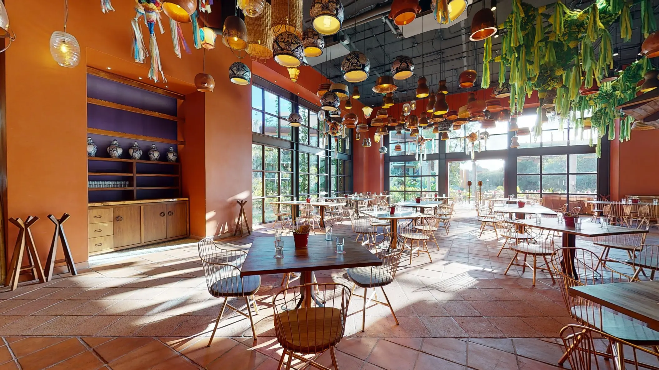 Bright, airy dining room with terracotta floors, floor-to-ceiling windows, and colorful hanging lights.