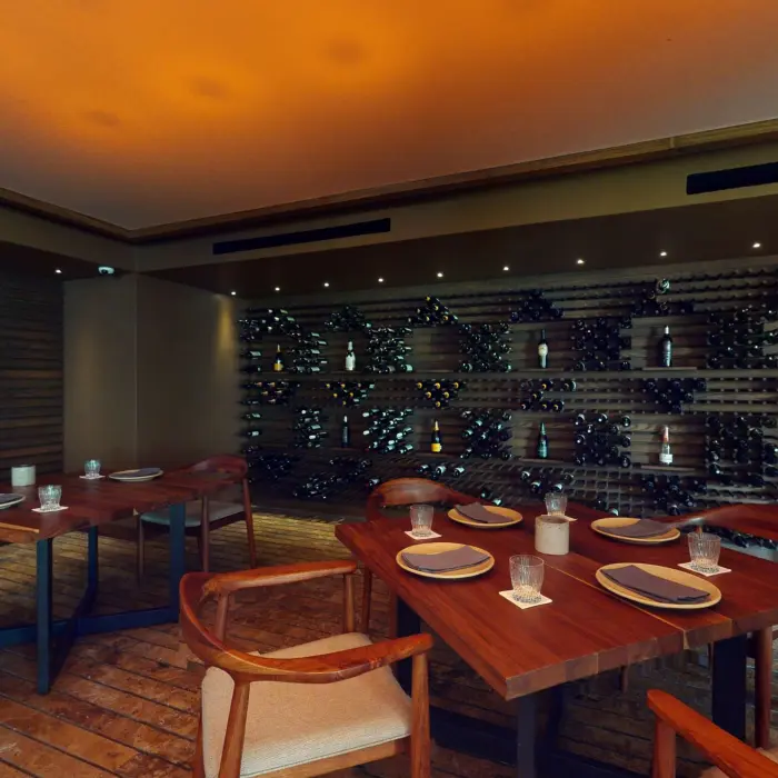 Intimate wine cellar dining room with wooden tables and a wall lined with decorative wine bottle racks.