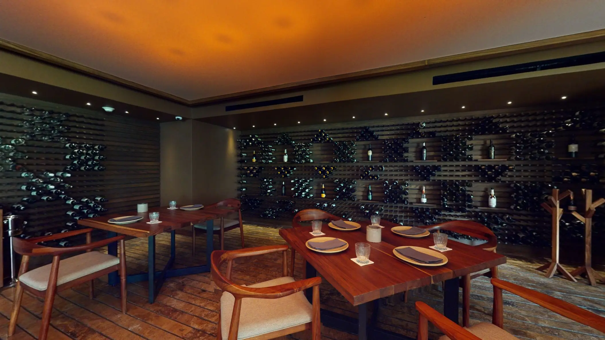 Intimate wine cellar dining room with wooden tables and a wall lined with decorative wine bottle racks.