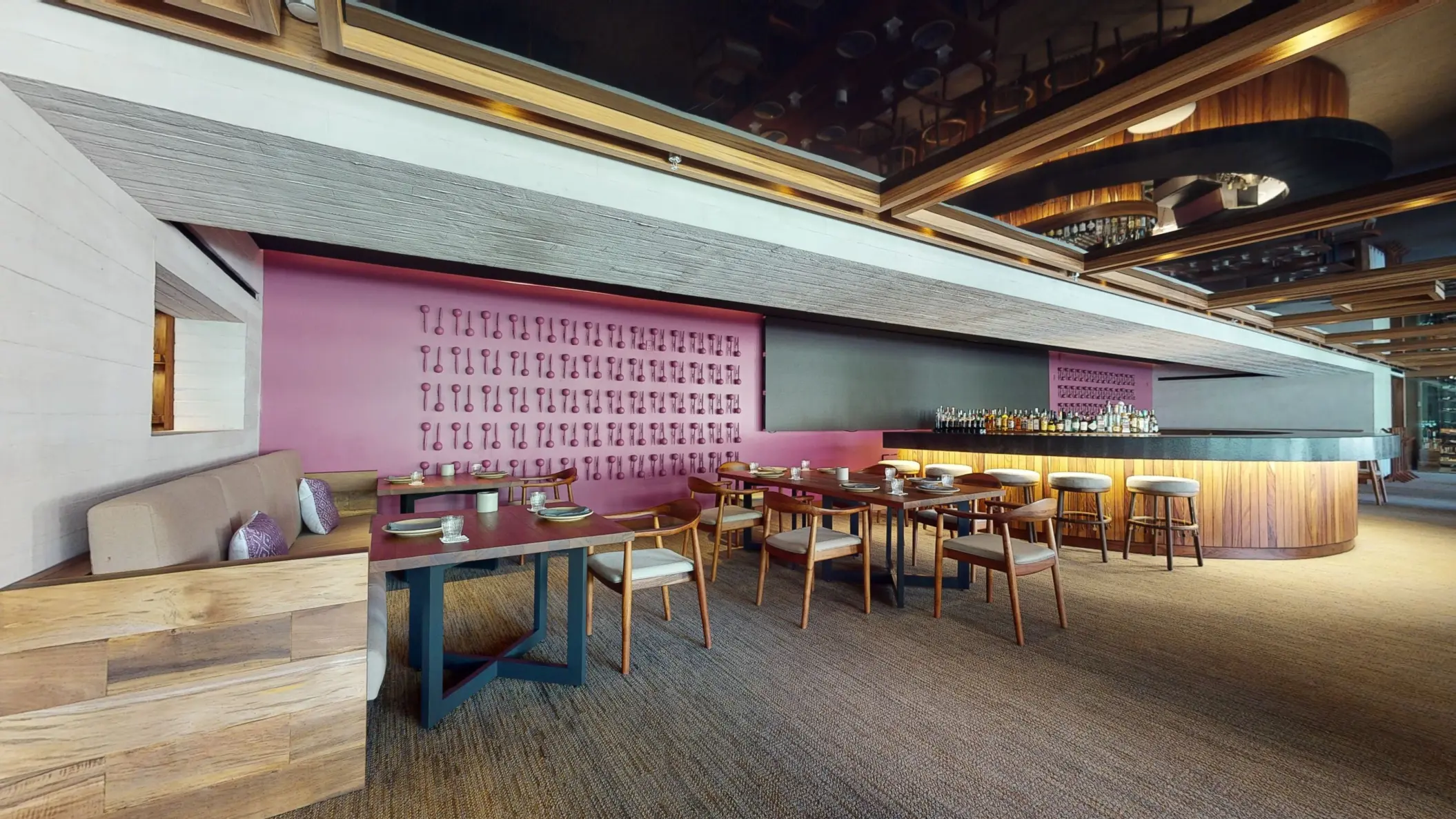 Contemporary restaurant with a pink accent wall, modern furniture, and a sleek bar under warm lighting.