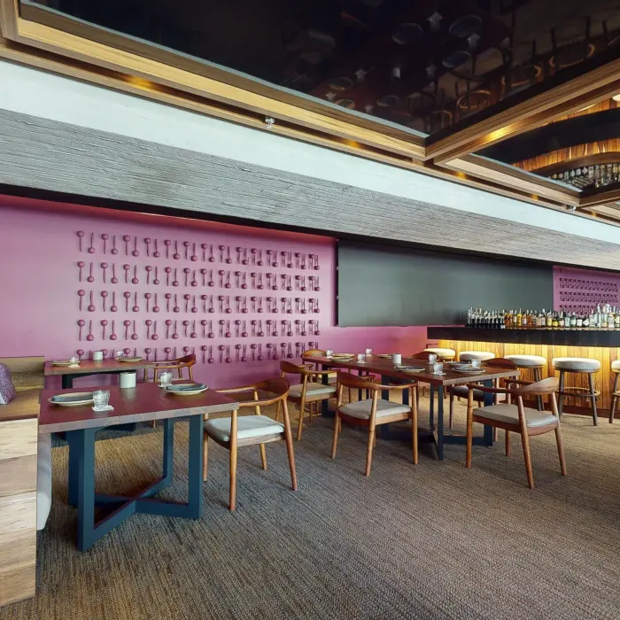 Contemporary restaurant with a pink accent wall, modern furniture, and a sleek bar under warm lighting.