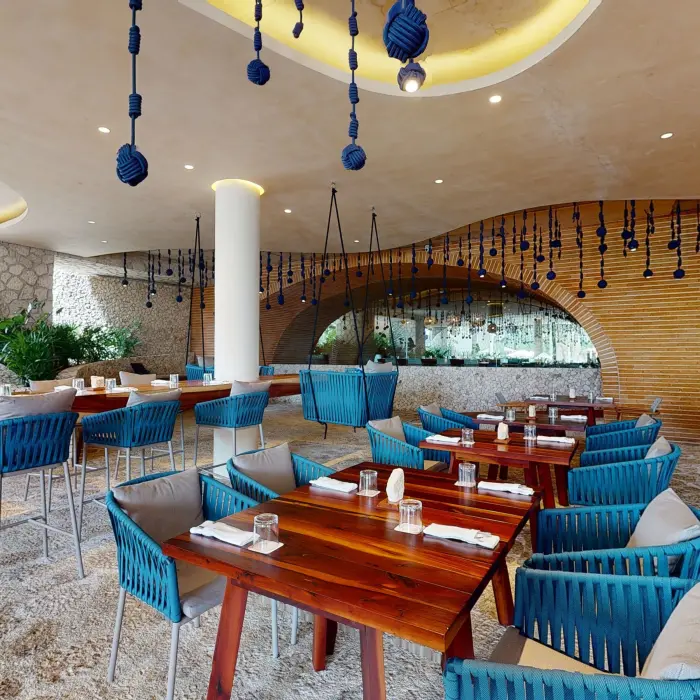 Open-air dining area with blue rope chairs, wooden tables, and creative hanging decor for a casual vibe.