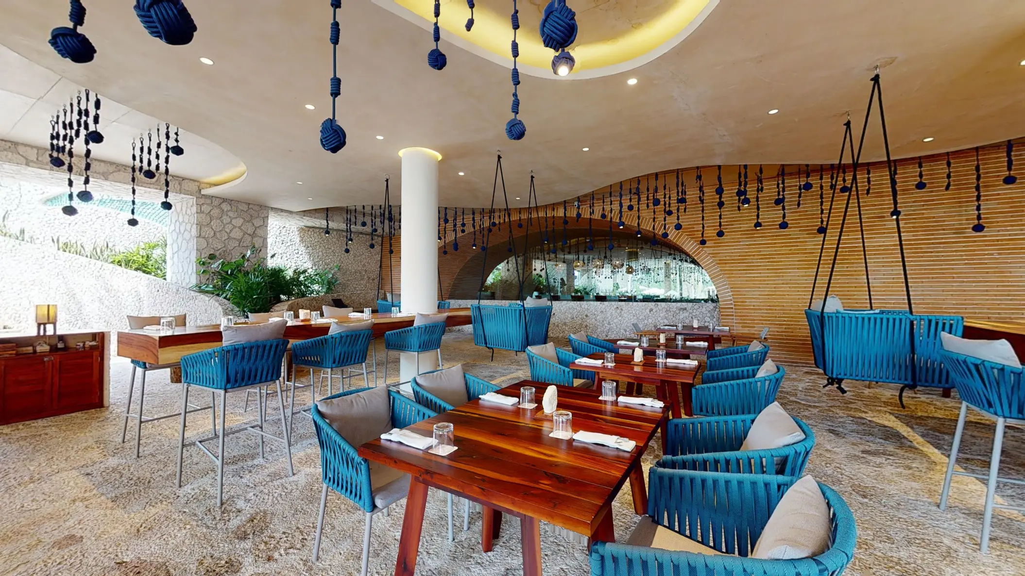 Open-air dining area with blue rope chairs, wooden tables, and creative hanging decor for a casual vibe.