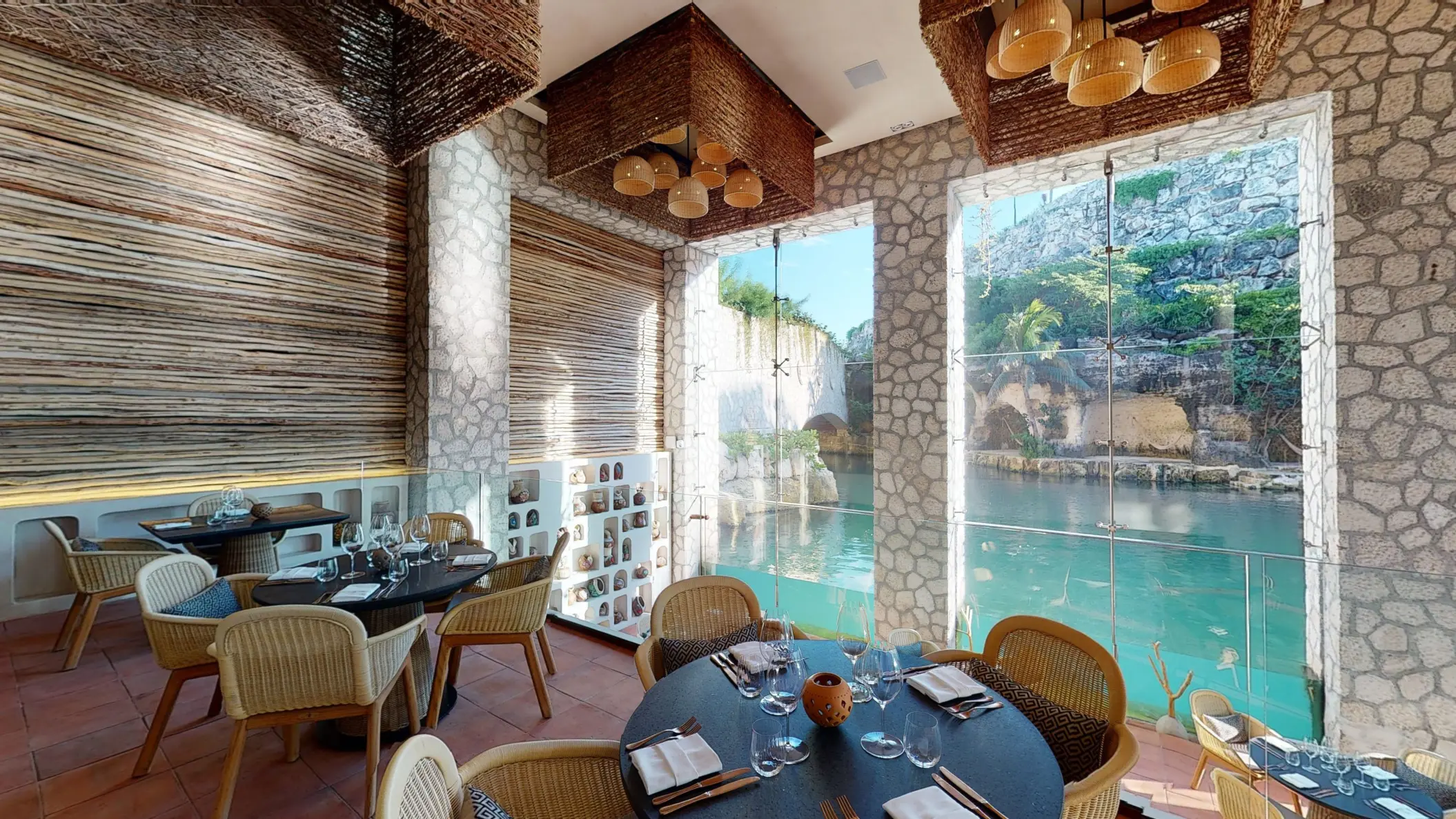Cozy riverside restaurant with stone walls, rattan chairs, and floor-to-ceiling windows overlooking the water.