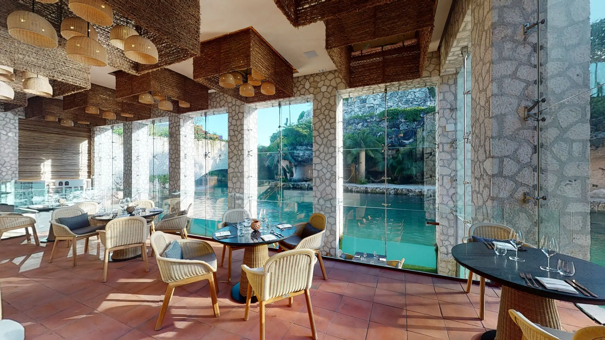 Scenic dining space with wide glass windows, river views, and warm woven lamps hanging from the ceiling.