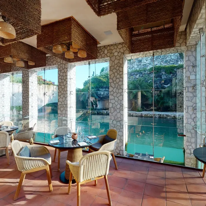 Scenic dining space with wide glass windows, river views, and warm woven lamps hanging from the ceiling.