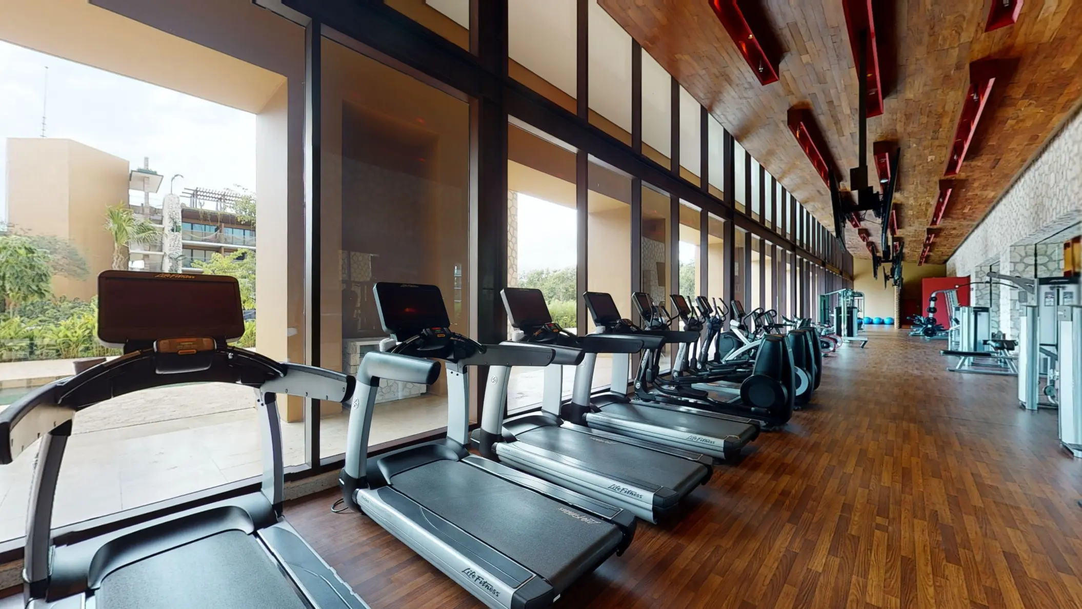 Spacious gym with treadmills, strength equipment, and floor-to-ceiling windows facing lush outdoor views.