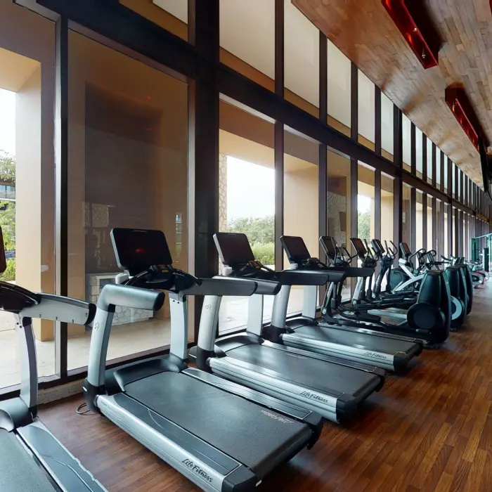 Spacious gym with treadmills, strength equipment, and floor-to-ceiling windows facing lush outdoor views.