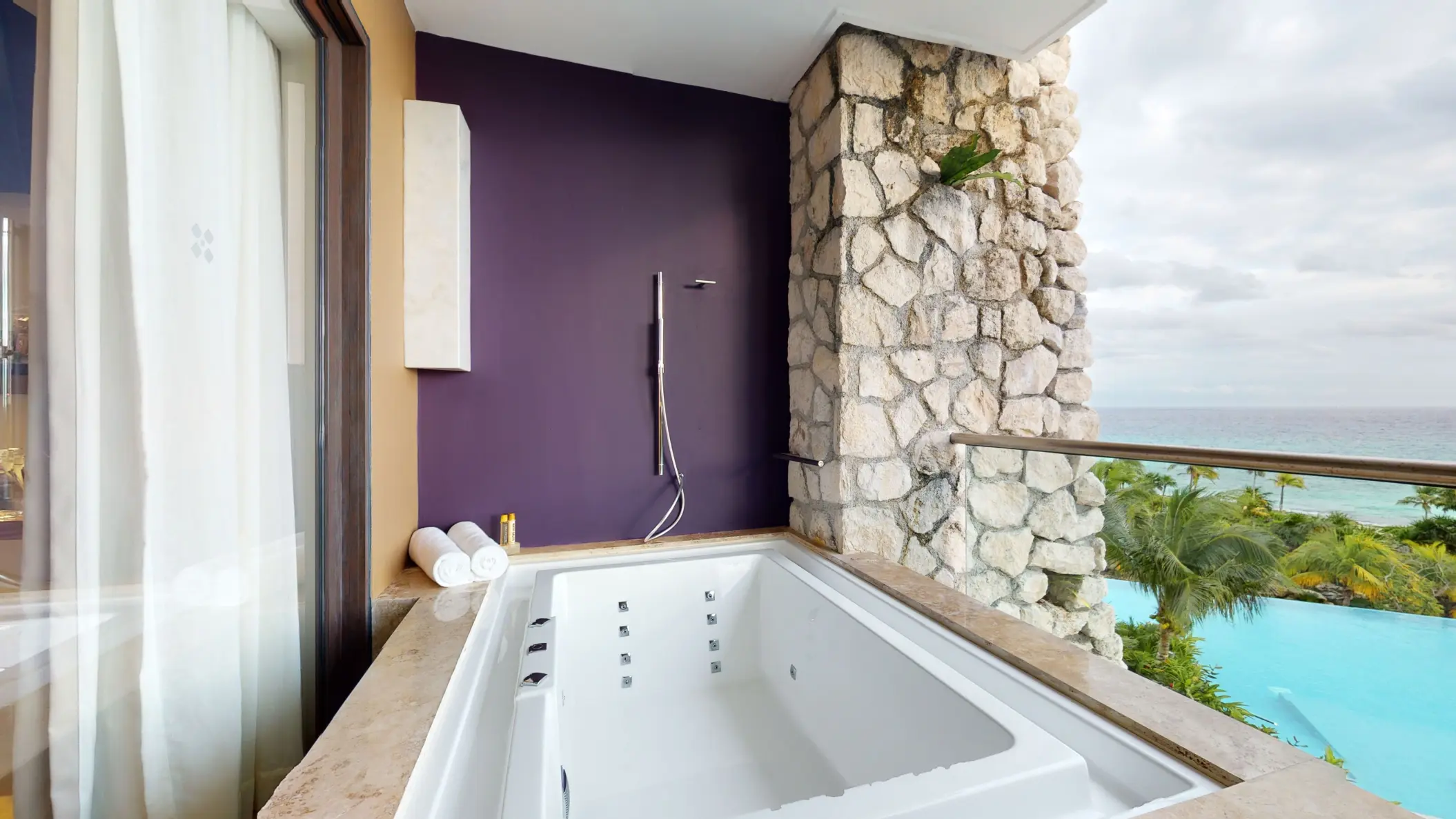 Private outdoor hot tub with ocean views, stone wall, and a deep purple accent wall for extra style.
