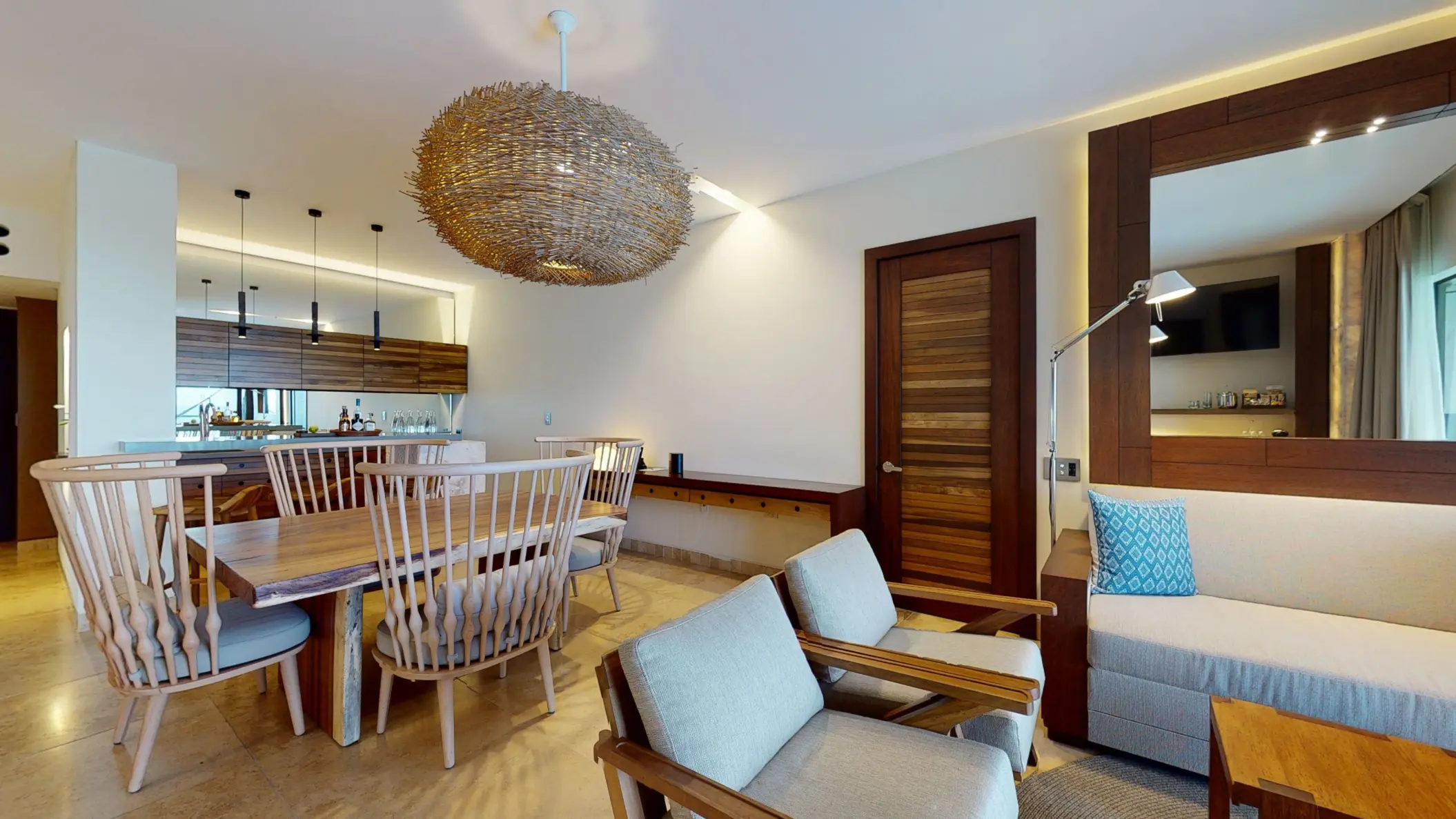 Elegant dining area with wooden chairs, woven pendant light, and soft-toned lounge in a luxury suite.