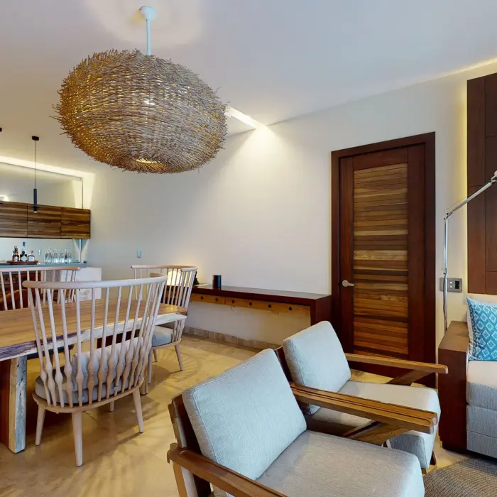 Elegant dining area with wooden chairs, woven pendant light, and soft-toned lounge in a luxury suite.