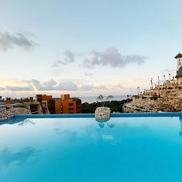 Infinity rooftop pool at sunset with panoramic ocean views and chapel perched on stone terrace.