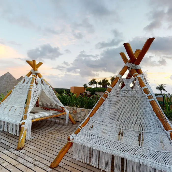 Handcrafted macramé daybeds under wooden pergola with ocean views at Hotel Xcaret Arte rooftop.