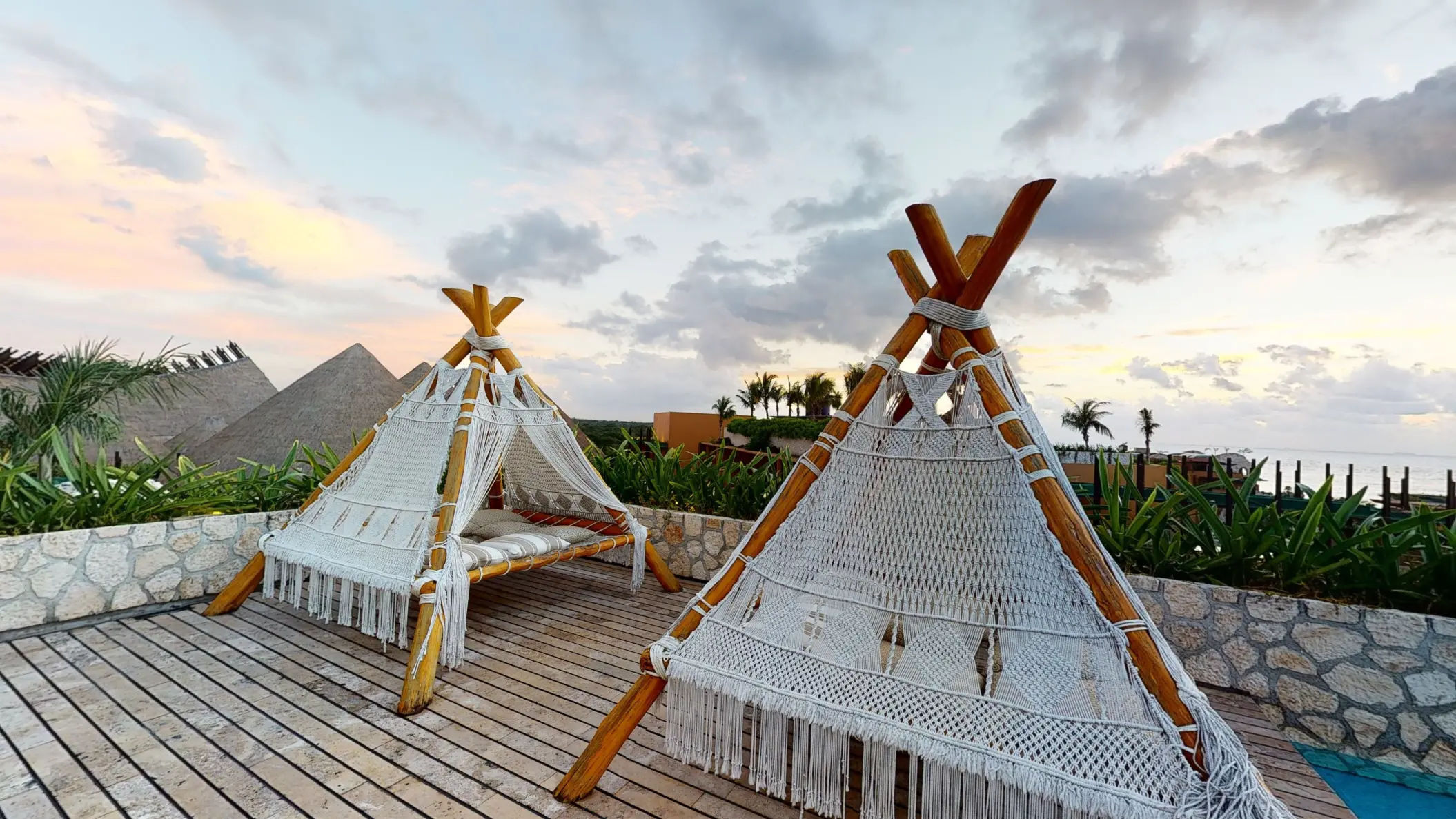 Handcrafted macramé daybeds under wooden pergola with ocean views at Hotel Xcaret Arte rooftop.