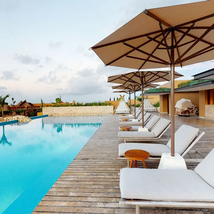 Infinity pool with modern loungers and umbrellas beside chapel at Hotel Xcaret Arte rooftop deck.