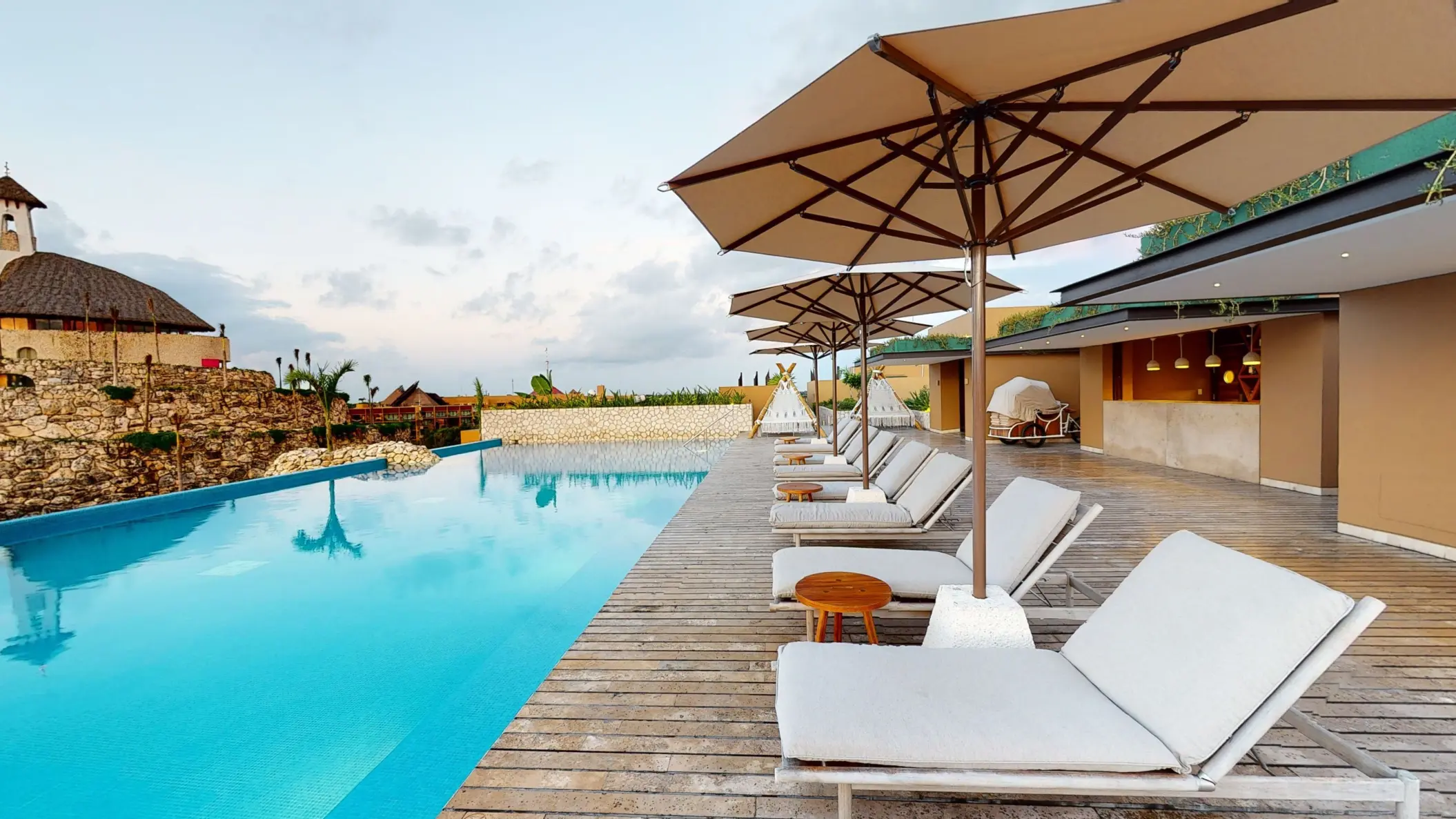 Infinity pool with modern loungers and umbrellas beside chapel at Hotel Xcaret Arte rooftop deck.