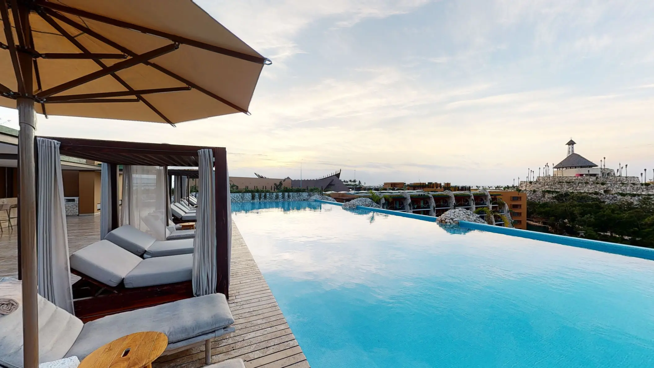 Infinity pool with sunbeds and panoramic views of Hotel Xcaret Arte’s chapel and surroundings.