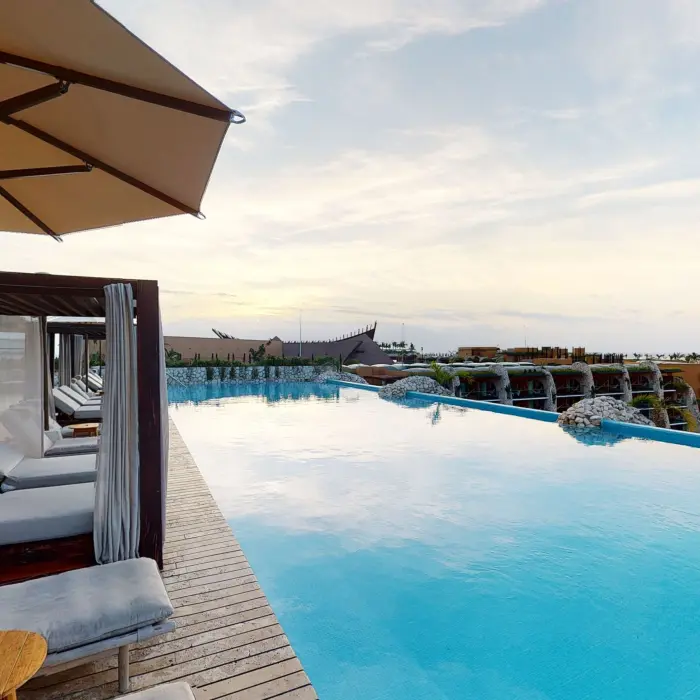 Infinity pool with sunbeds and panoramic views of Hotel Xcaret Arte’s chapel and surroundings.