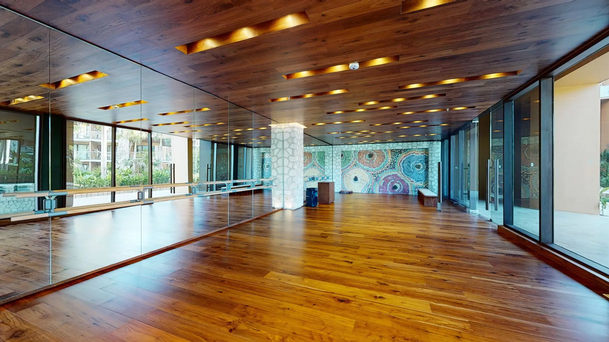 Bright dance or yoga studio with mirrored wall, hardwood floors, and mosaic art under modern ceiling lights.
