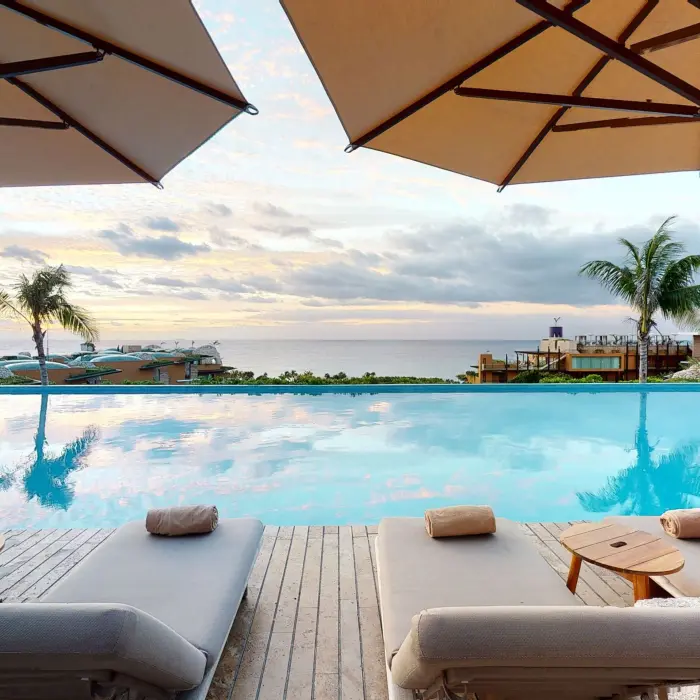 Oceanview infinity pool with padded loungers and umbrellas, perfect for sunset relaxation.