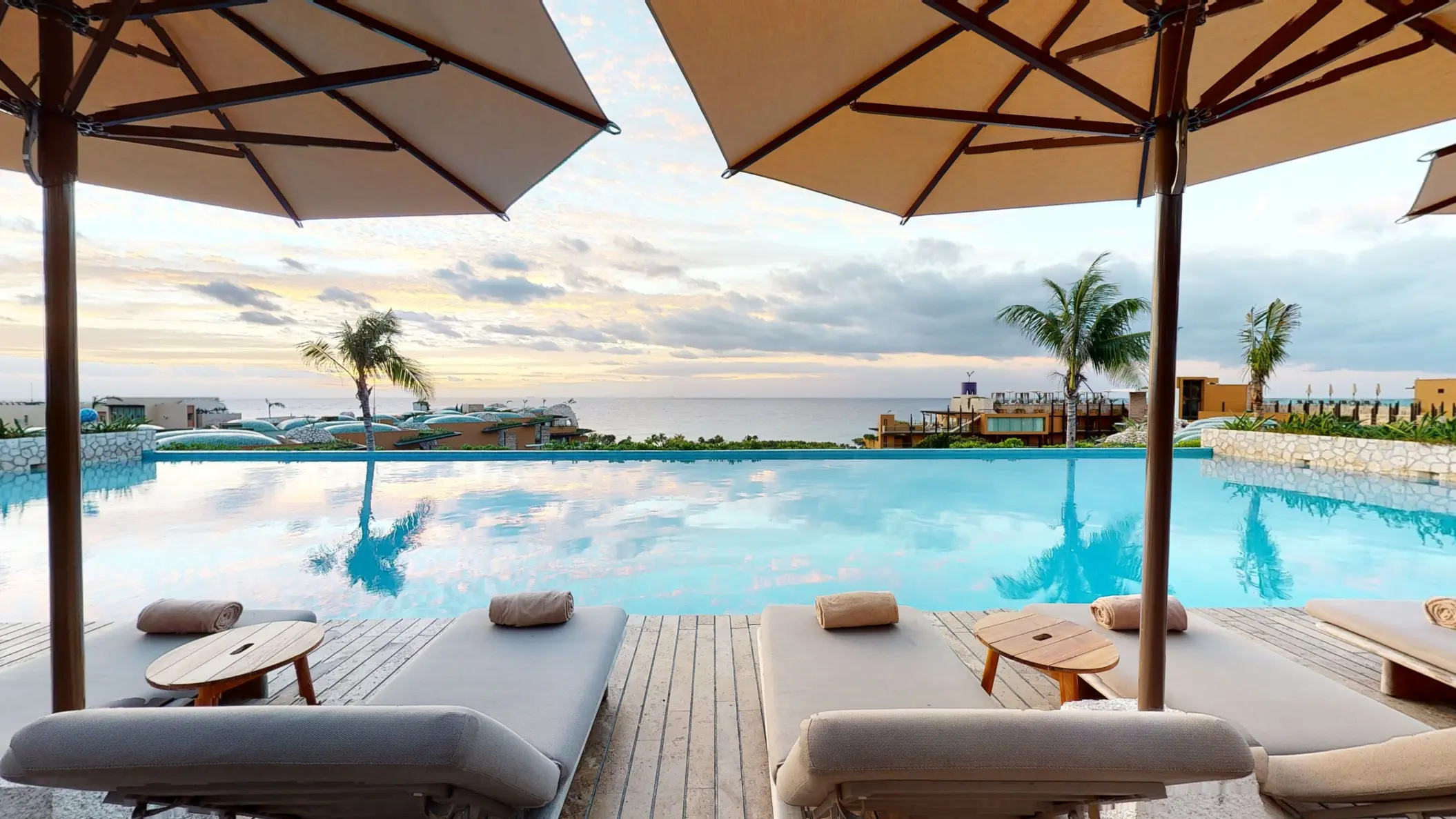 Oceanview infinity pool with padded loungers and umbrellas, perfect for sunset relaxation.